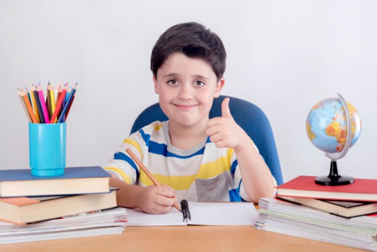 Masasında kalemleri ve küresiyle ders çalışırken gülümseyen çocuk