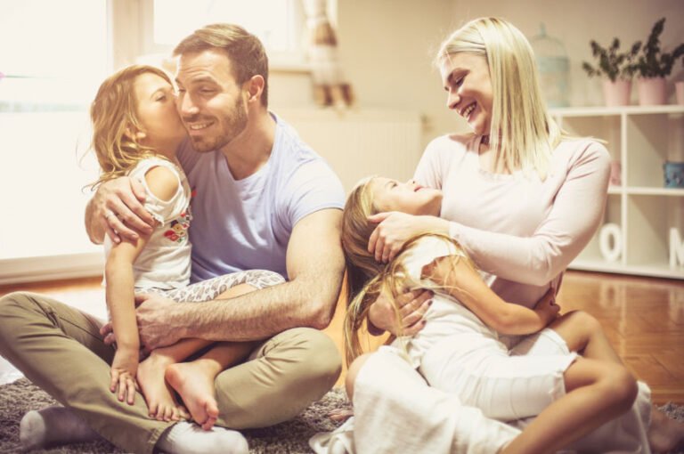 Oturma odasında sarılıp gülüşen anne, baba ve iki çocuk